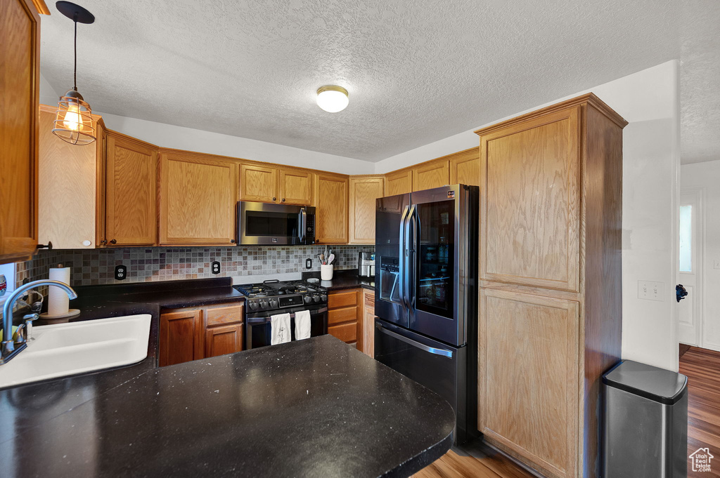 Kitchen featuring hardwood / wood-style floors, pendant lighting, black appliances, backsplash, and sink