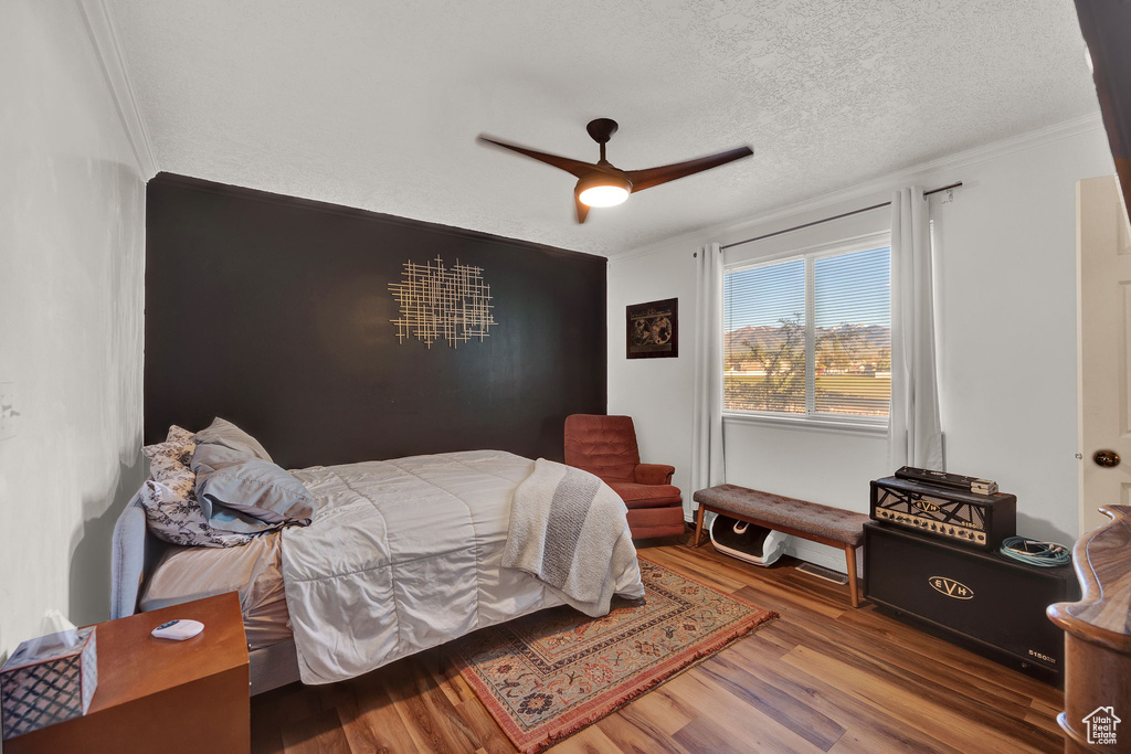 Bedroom with a textured ceiling, ornamental molding, ceiling fan, and dark hardwood / wood-style flooring