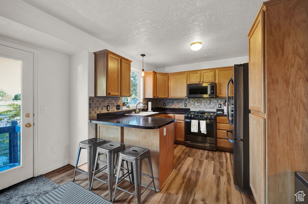 Kitchen featuring hardwood / wood-style floors, kitchen peninsula, fridge, pendant lighting, and black gas stove