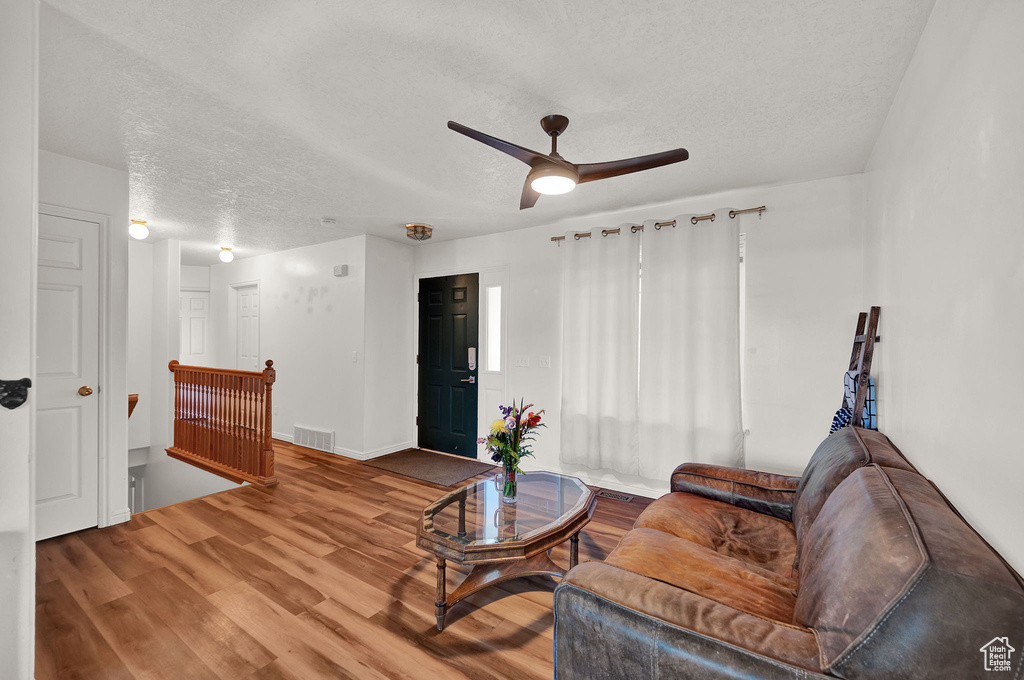 Living room featuring ceiling fan, a textured ceiling, and wood-type flooring