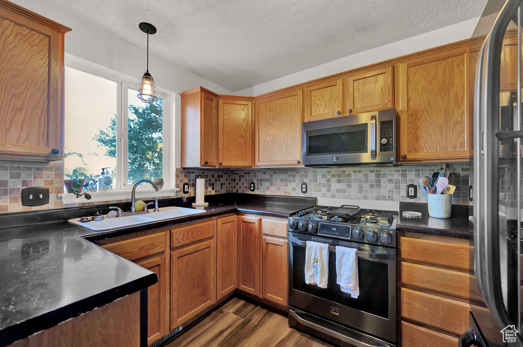 Kitchen featuring appliances with stainless steel finishes, backsplash, wood-type flooring, and pendant lighting