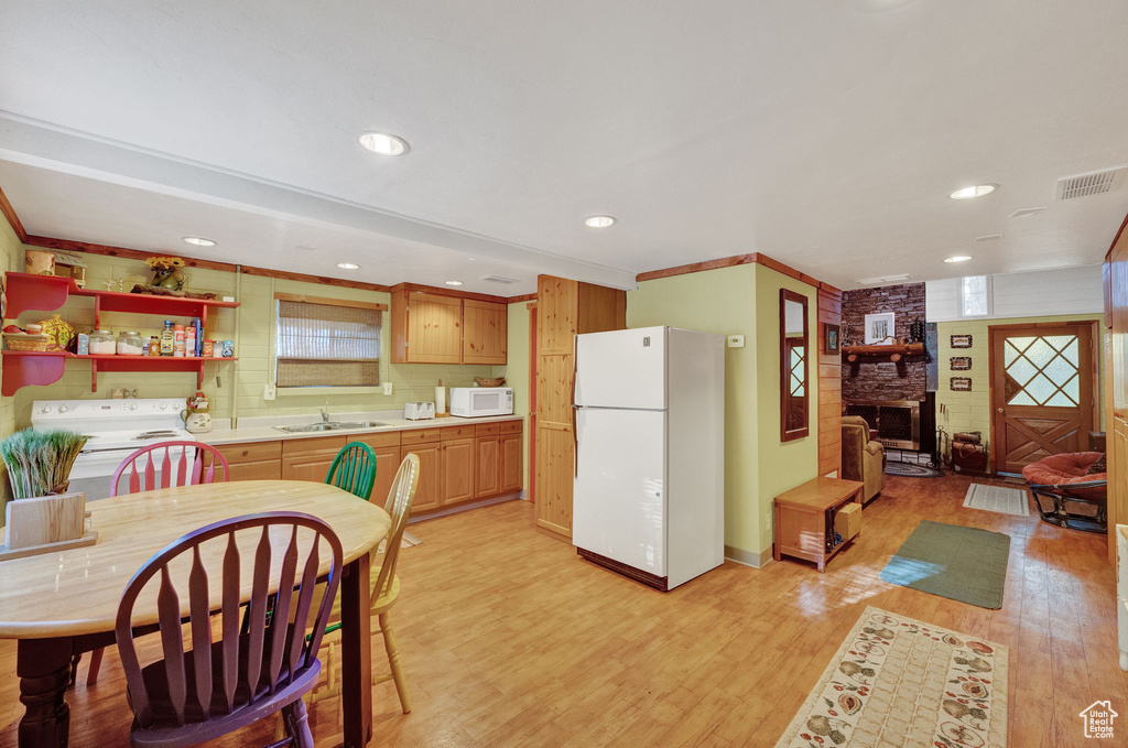 Kitchen featuring brick wall, a fireplace, light wood-type flooring, sink, and white appliances