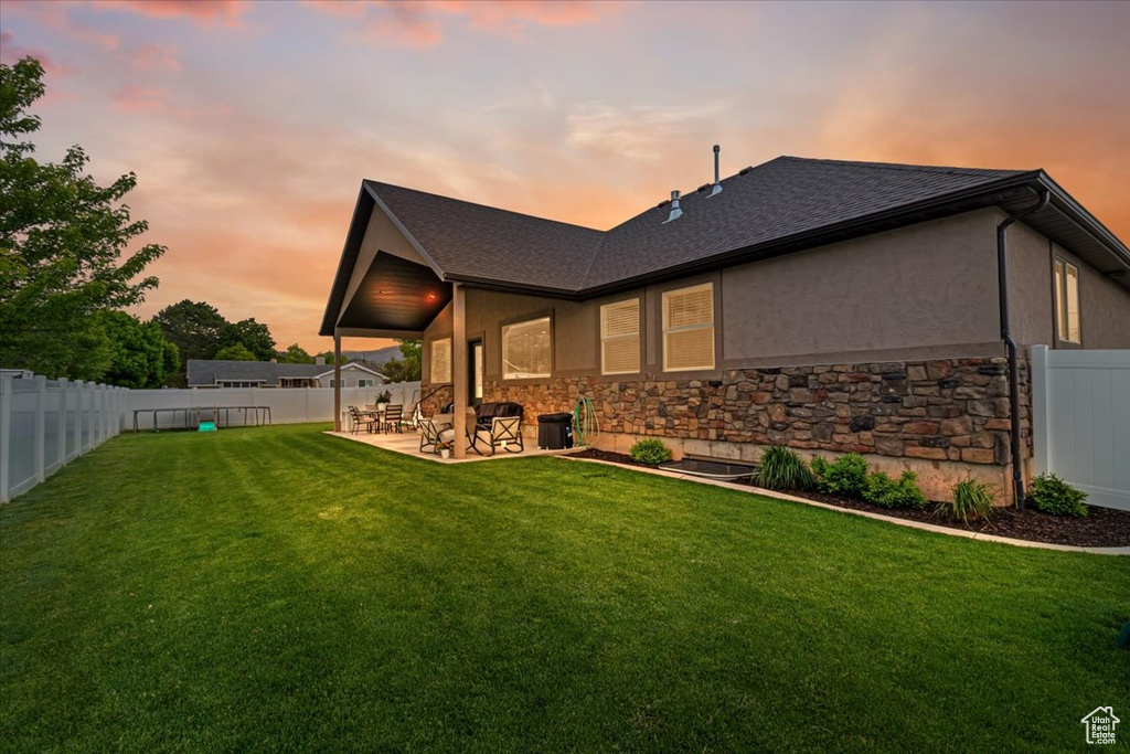 Back house at dusk featuring a patio area and a lawn