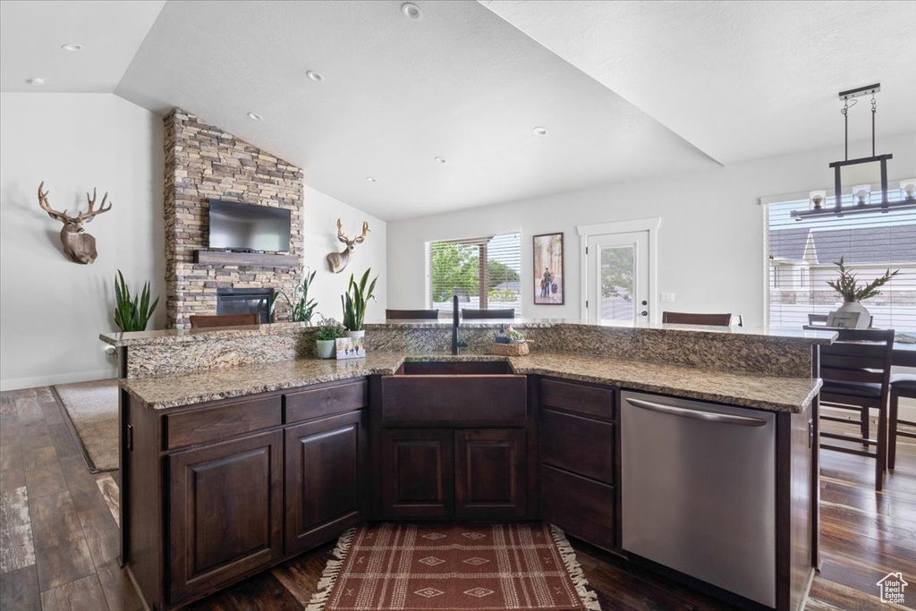 Kitchen featuring vaulted ceiling, dark brown cabinetry, a fireplace, stainless steel dishwasher, and dark wood-type flooring