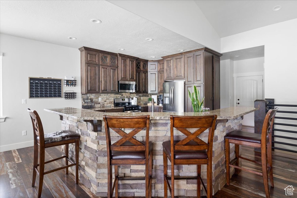 Kitchen with light stone countertops, tasteful backsplash, stainless steel appliances, dark wood-type flooring, and a kitchen bar