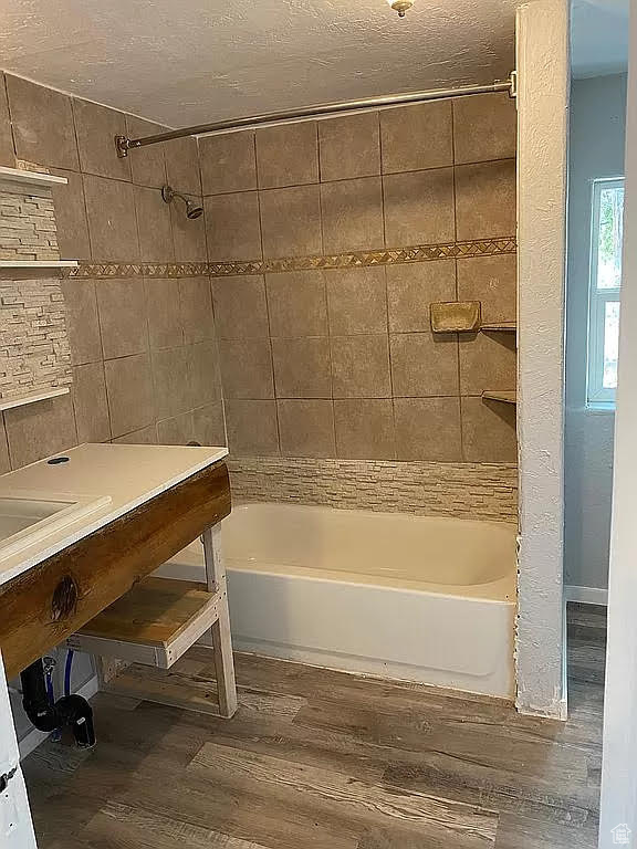 Bathroom featuring tile walls, a textured ceiling, wood-type flooring, and tiled shower / bath