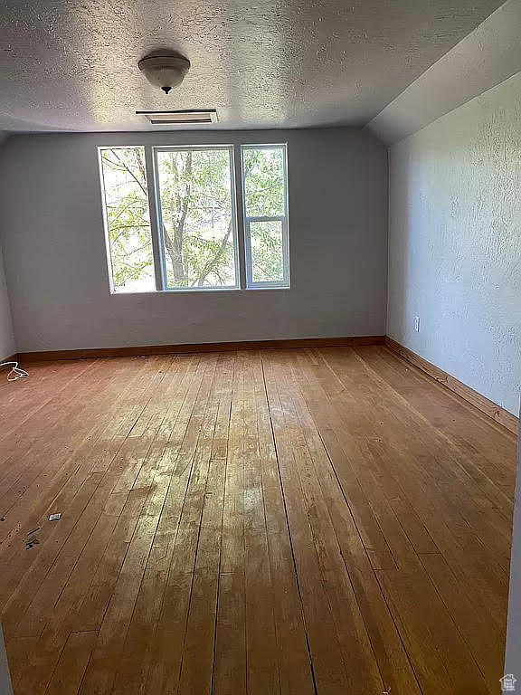 Unfurnished room featuring a textured ceiling, vaulted ceiling, and hardwood / wood-style floors