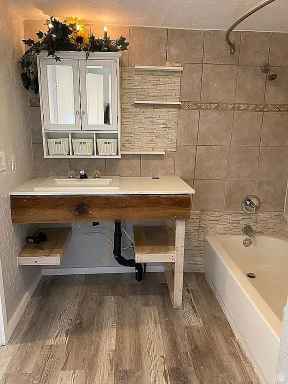 Bathroom with tiled shower / bath combo, a textured ceiling, hardwood / wood-style flooring, and vanity