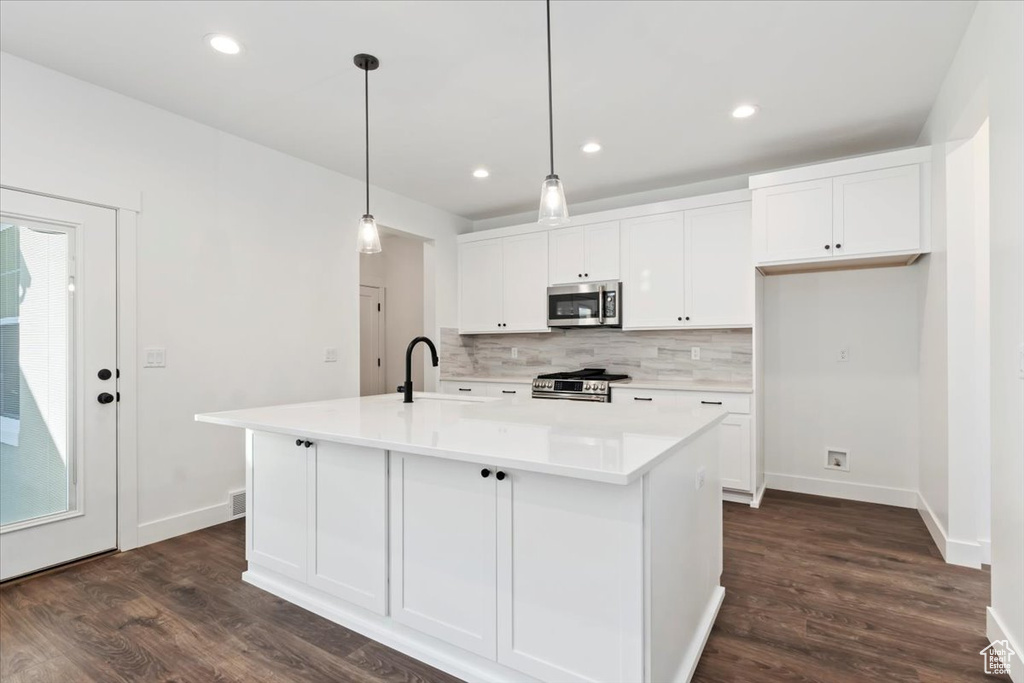 Kitchen with sink, dark hardwood / wood-style floors, pendant lighting, a kitchen island with sink, and appliances with stainless steel finishes