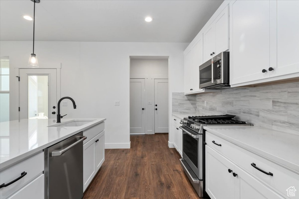 Kitchen with dark wood-type flooring, sink, appliances with stainless steel finishes, decorative light fixtures, and white cabinetry