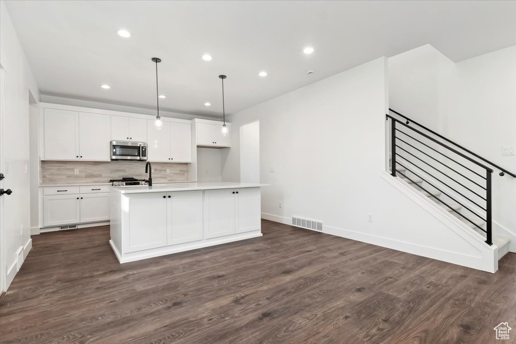 Kitchen with a center island with sink, white cabinetry, hanging light fixtures, and dark wood-type flooring