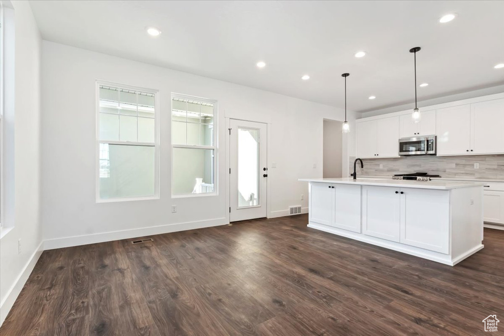 Kitchen featuring dark wood-type flooring, an island with sink, pendant lighting, white cabinets, and range