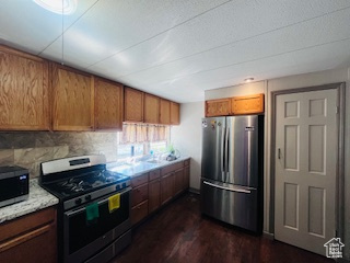 Kitchen featuring dark hardwood / wood-style flooring, backsplash, light stone counters, and stainless steel appliances