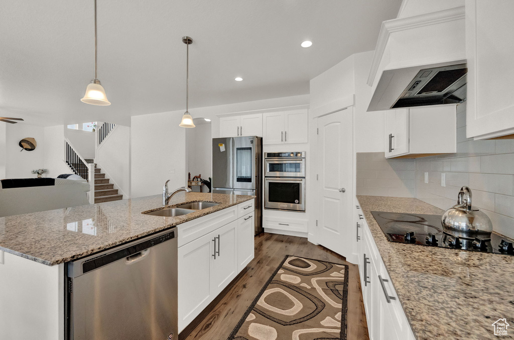 Kitchen featuring a center island with sink, stainless steel appliances, dark hardwood / wood-style floors, backsplash, and sink