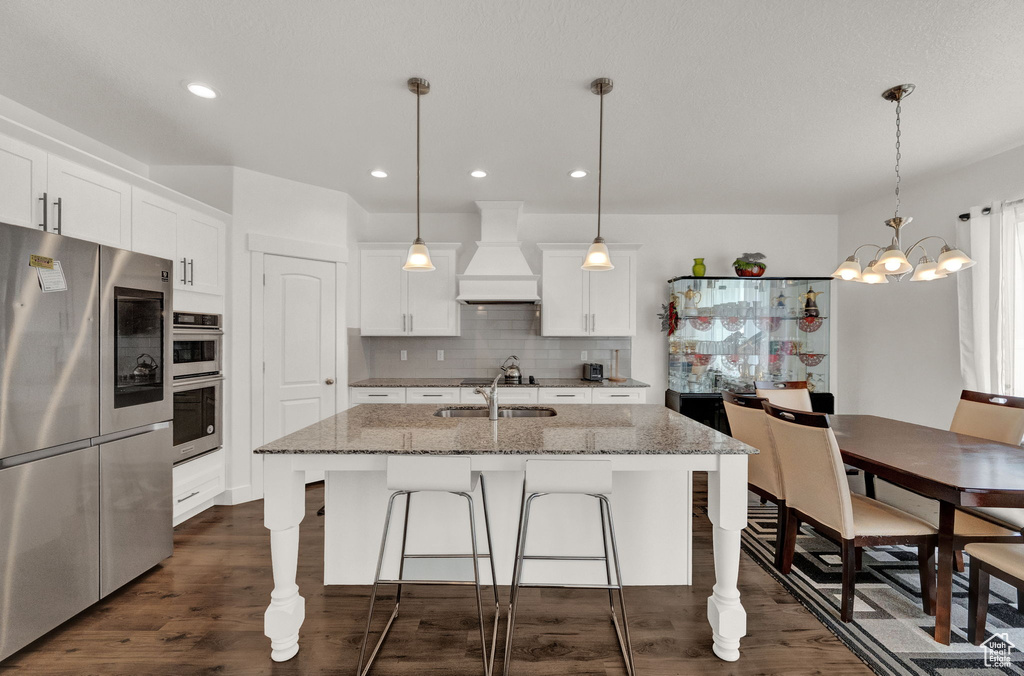 Kitchen featuring decorative light fixtures, custom range hood, dark hardwood / wood-style floors, stainless steel appliances, and backsplash