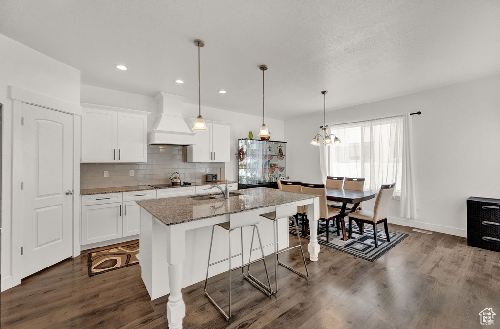 Kitchen with dark hardwood / wood-style flooring, backsplash, stone counters, a kitchen island with sink, and custom exhaust hood