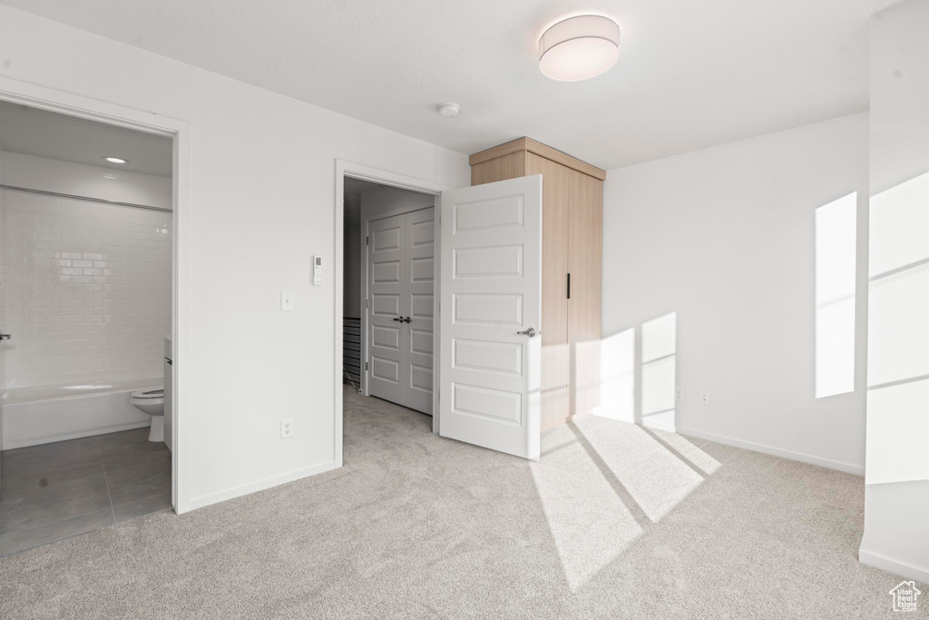 Unfurnished bedroom with connected bathroom and light colored carpet