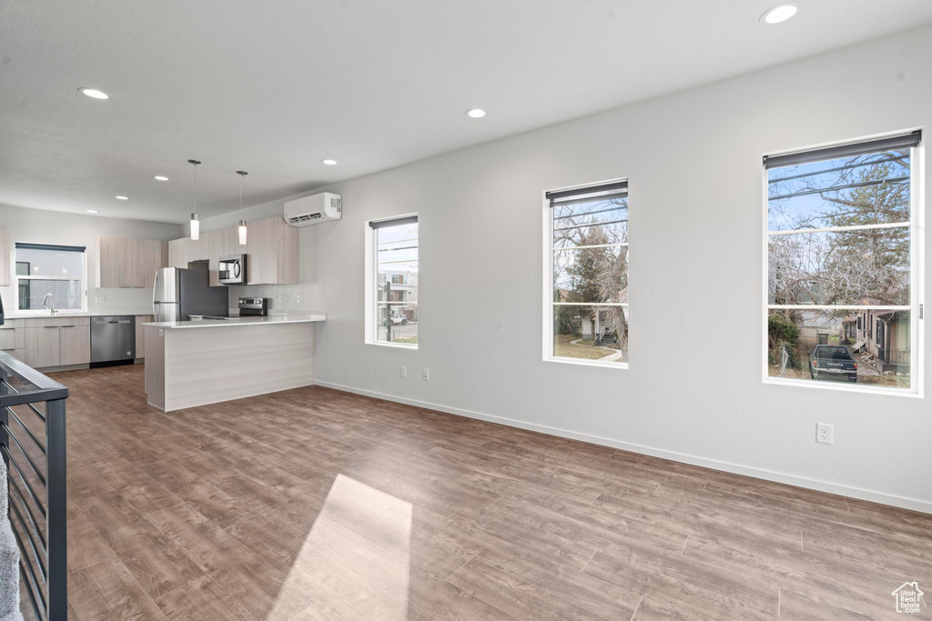 Kitchen with wood-type flooring, a healthy amount of sunlight, a wall mounted AC, and appliances with stainless steel finishes