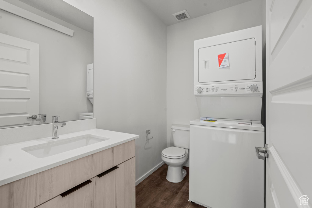 Bathroom with wood-type flooring, large vanity, toilet, and stacked washer / drying machine