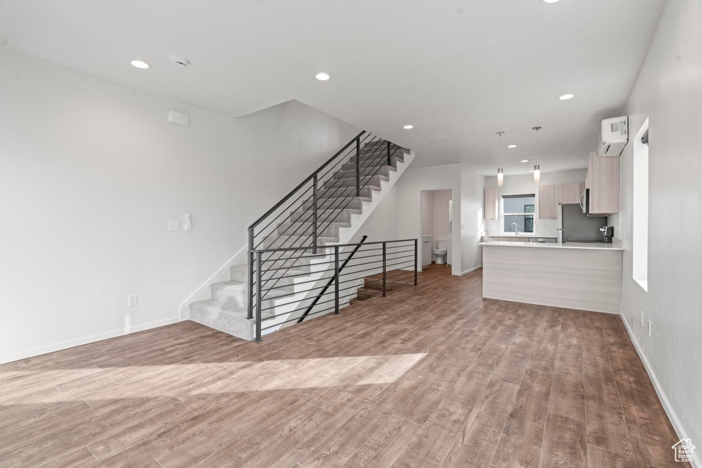 Unfurnished living room with a wall mounted air conditioner and light hardwood / wood-style flooring