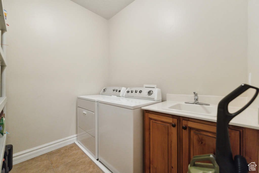 Clothes washing area featuring cabinets, sink, washing machine and dryer, and light tile floors