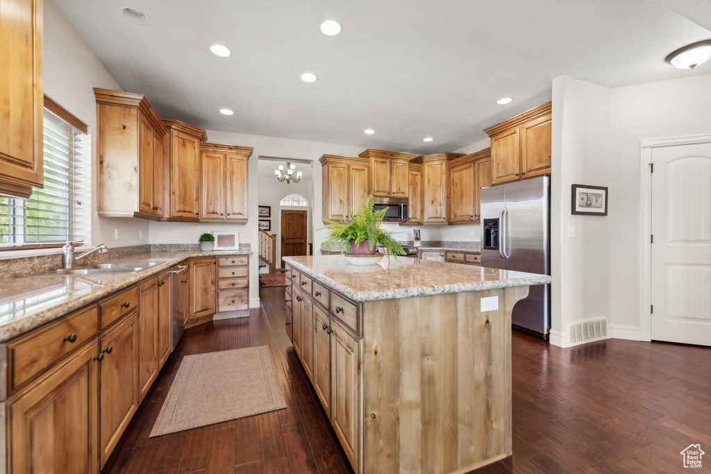 Kitchen featuring light stone countertops, dark wood-type flooring, a kitchen island, and appliances with stainless steel finishes