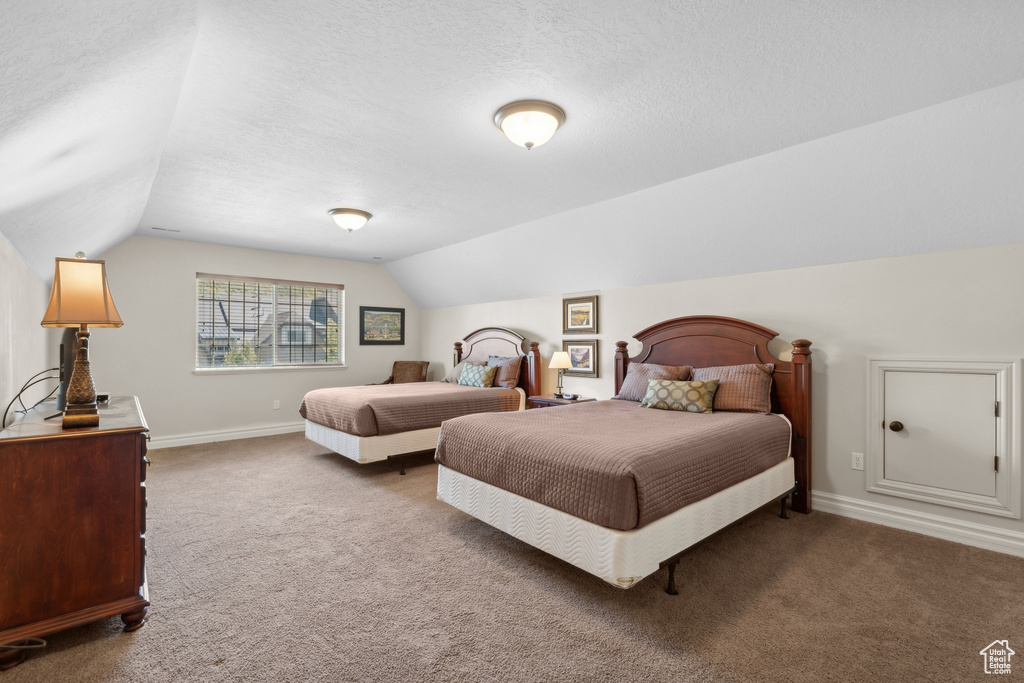 Carpeted bedroom featuring a textured ceiling and vaulted ceiling