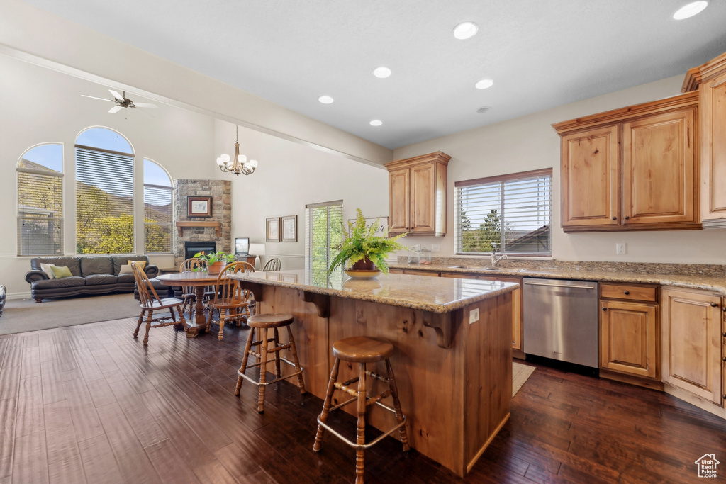 Kitchen with dishwasher, a fireplace, ceiling fan with notable chandelier, dark hardwood / wood-style flooring, and a kitchen island