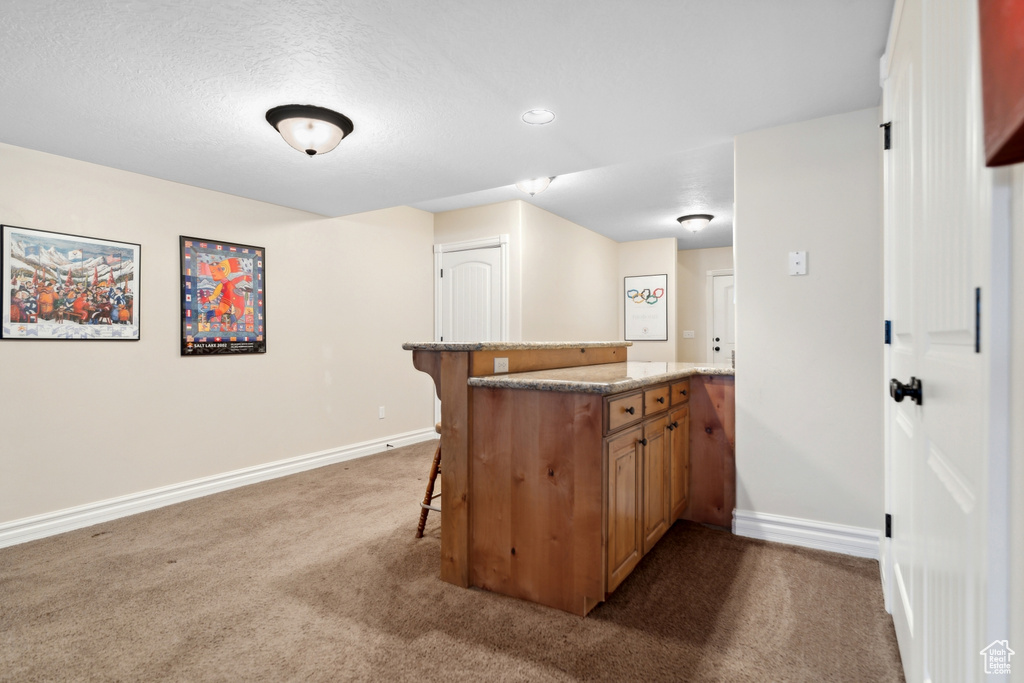 Kitchen featuring a breakfast bar, a textured ceiling, carpet, and stone counters