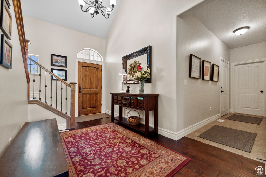 Entrance foyer with dark hardwood / wood-style floors, high vaulted ceiling, and an inviting chandelier