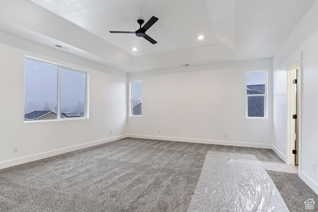 Empty room with a raised ceiling, carpet, and ceiling fan