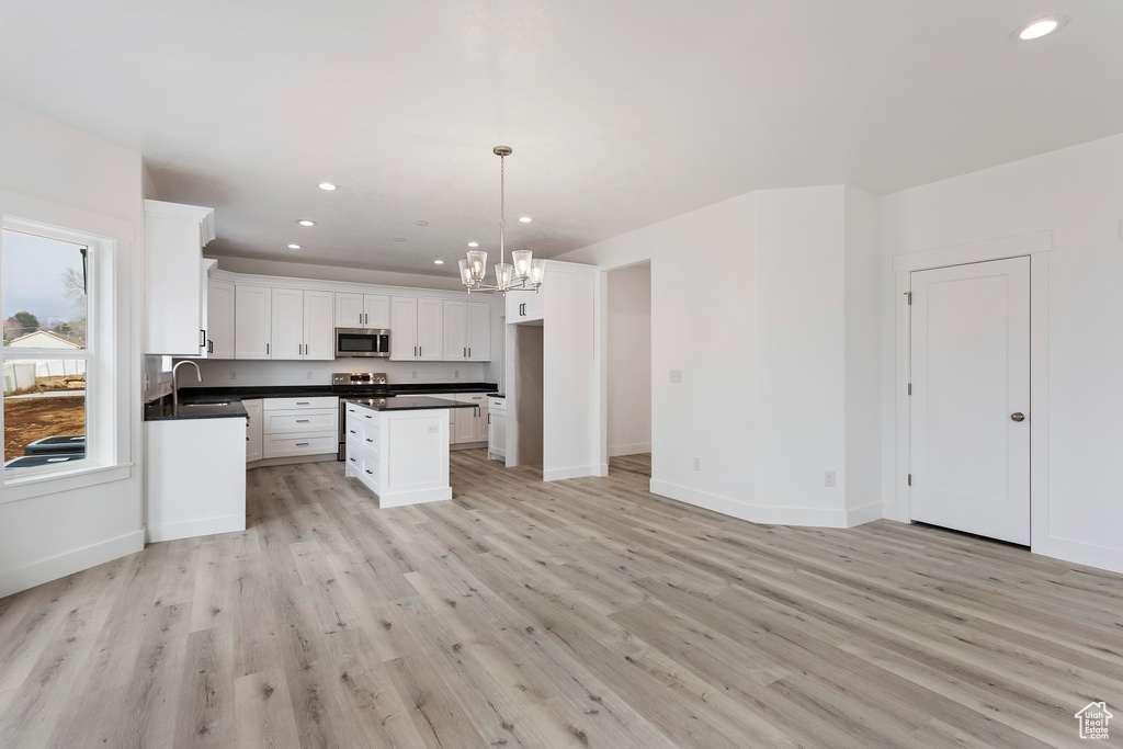 Kitchen featuring light hardwood / wood-style floors, pendant lighting, a kitchen island, sink, and white cabinets