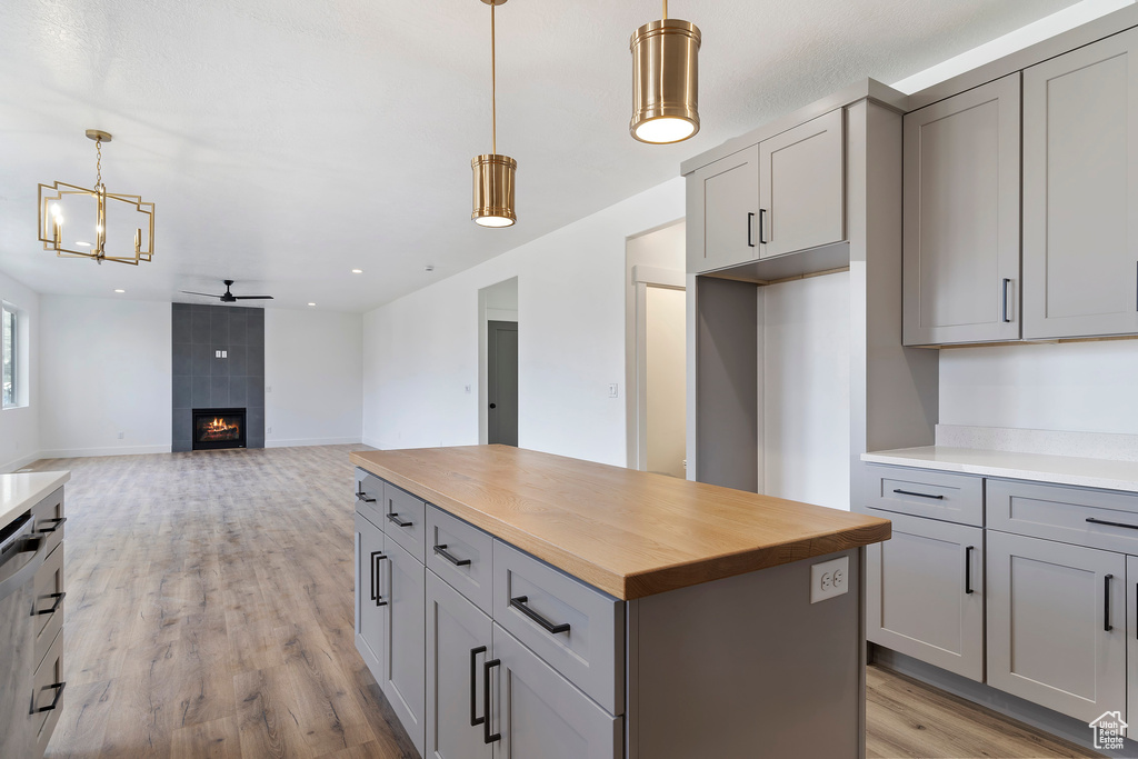 Kitchen with decorative light fixtures, a kitchen island, light wood-type flooring, wooden counters, and a tile fireplace