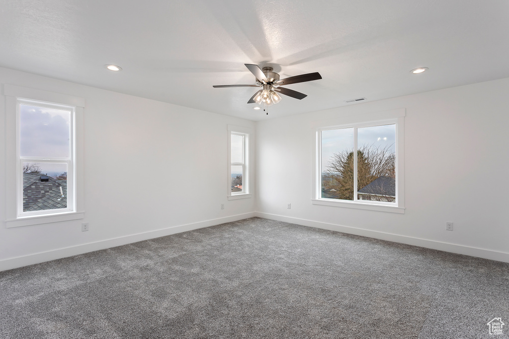 Empty room with plenty of natural light, ceiling fan, and carpet floors