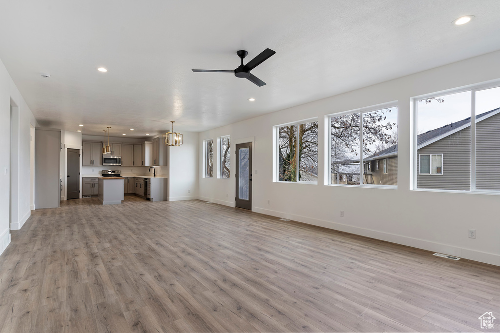 Unfurnished living room with sink, plenty of natural light, light hardwood / wood-style flooring, and ceiling fan with notable chandelier