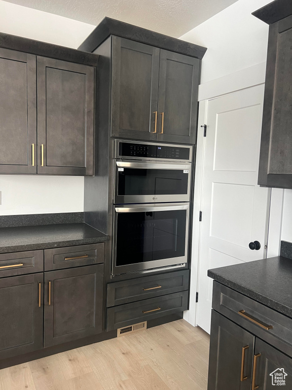 Kitchen with light hardwood / wood-style floors, stainless steel double oven, and dark brown cabinetry