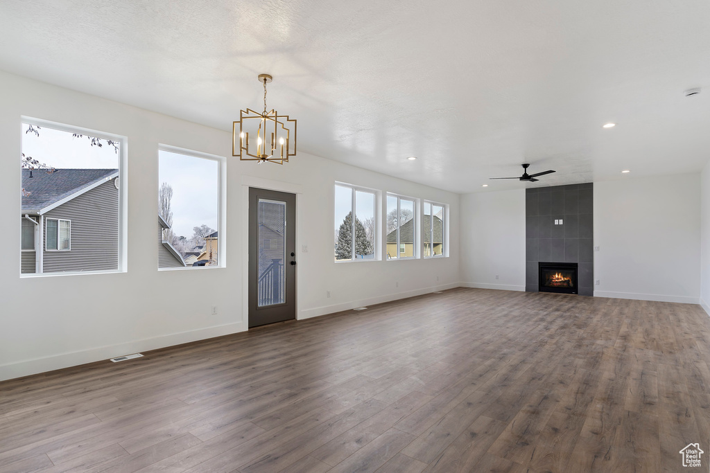 Unfurnished living room with a tiled fireplace, hardwood / wood-style flooring, tile walls, and ceiling fan with notable chandelier