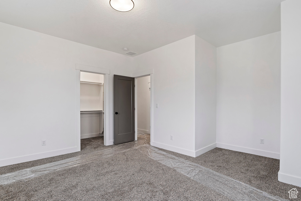 Unfurnished bedroom with a spacious closet, carpet flooring, and a closet