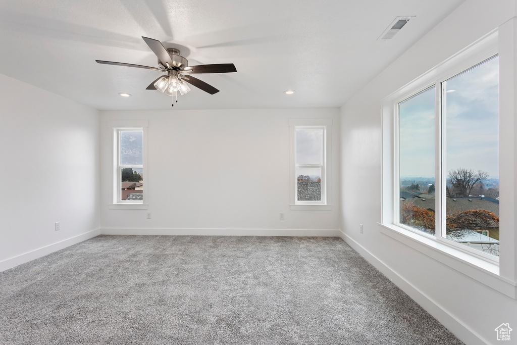 Carpeted spare room featuring a healthy amount of sunlight and ceiling fan