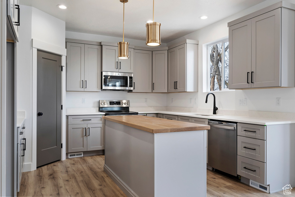 Kitchen with a kitchen island, stainless steel appliances, light wood-type flooring, and wooden counters