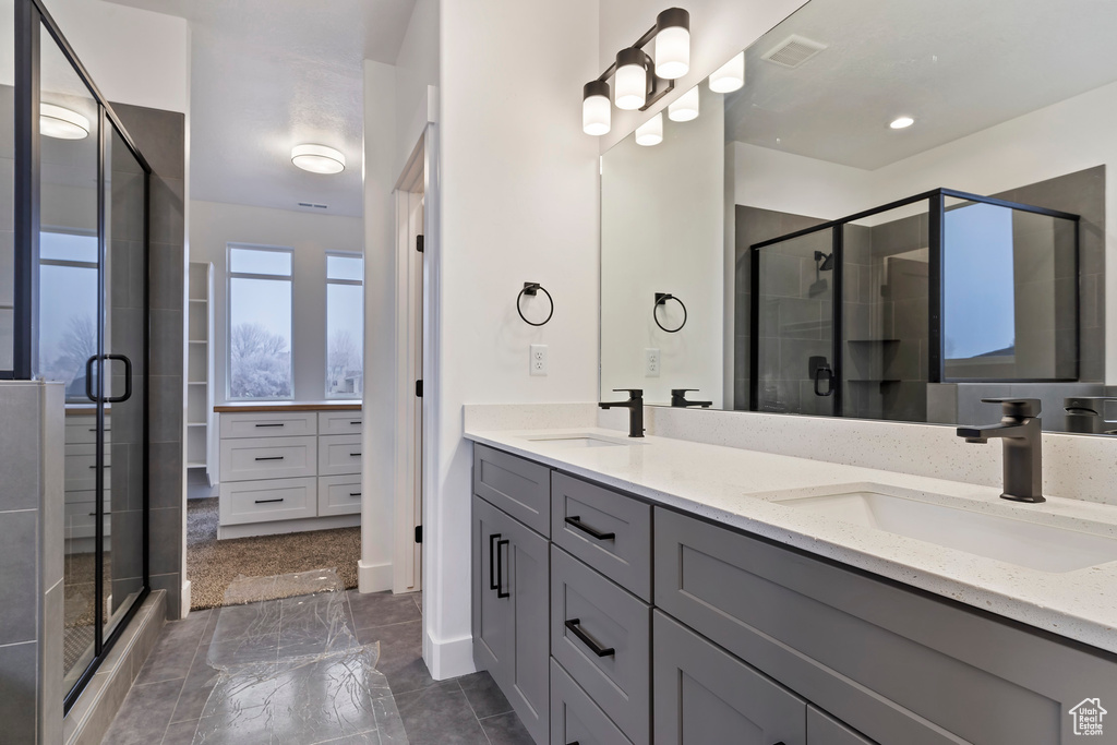 Bathroom featuring tile flooring, vanity with extensive cabinet space, an enclosed shower, and double sink