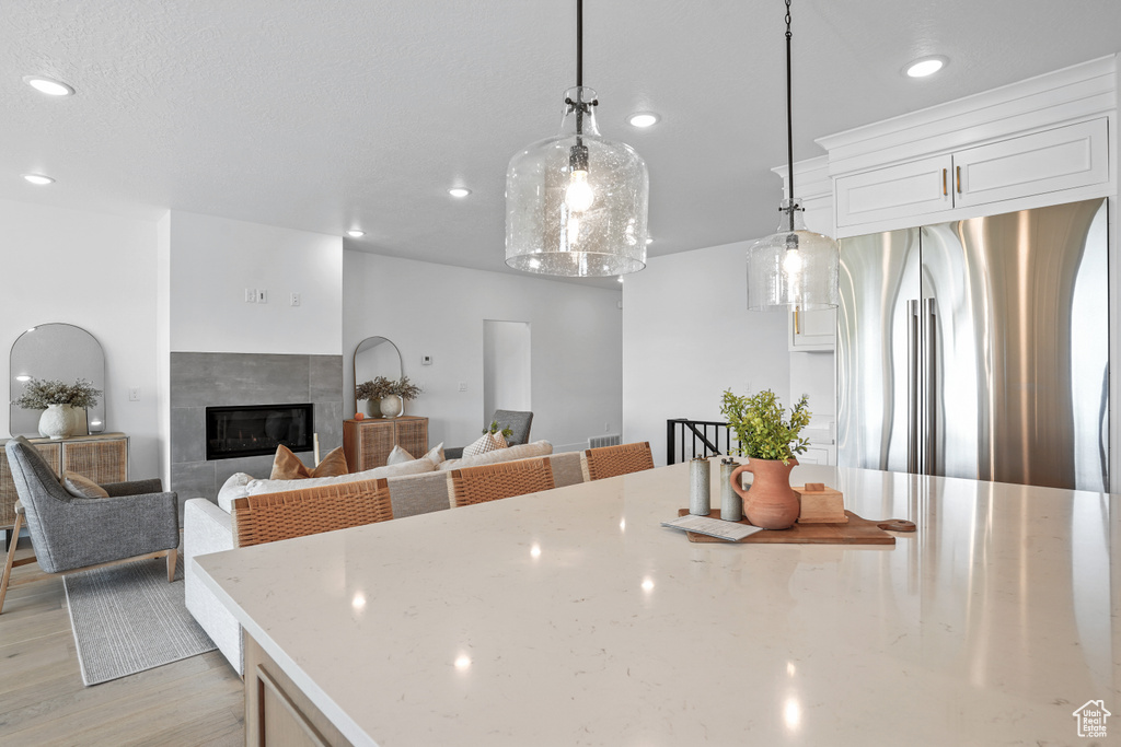 Kitchen with a tiled fireplace, light hardwood / wood-style floors, stainless steel fridge, decorative light fixtures, and white cabinetry