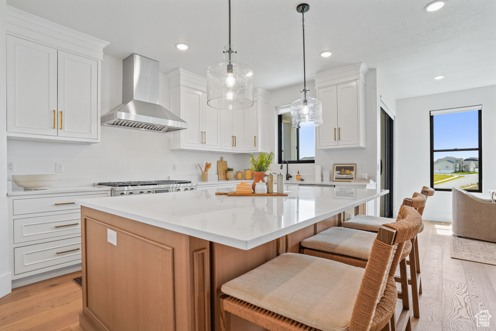 Kitchen featuring wall chimney range hood, a center island, a kitchen bar, and light wood-type flooring