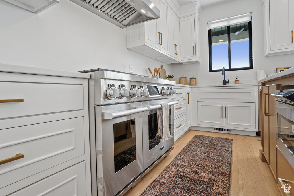 Kitchen with light hardwood / wood-style flooring, custom exhaust hood, range with two ovens, sink, and white cabinetry