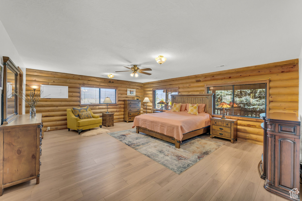 Bedroom with ceiling fan, rustic walls, light hardwood / wood-style flooring, and multiple windows