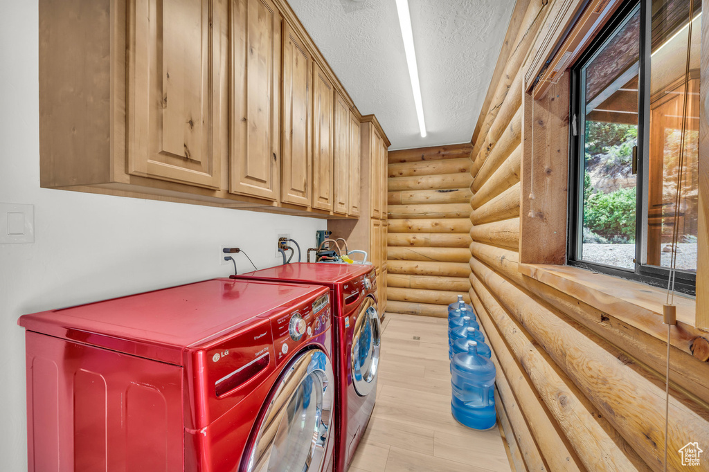 Laundry room with cabinets, light hardwood / wood-style flooring, washing machine and dryer, log walls, and a textured ceiling