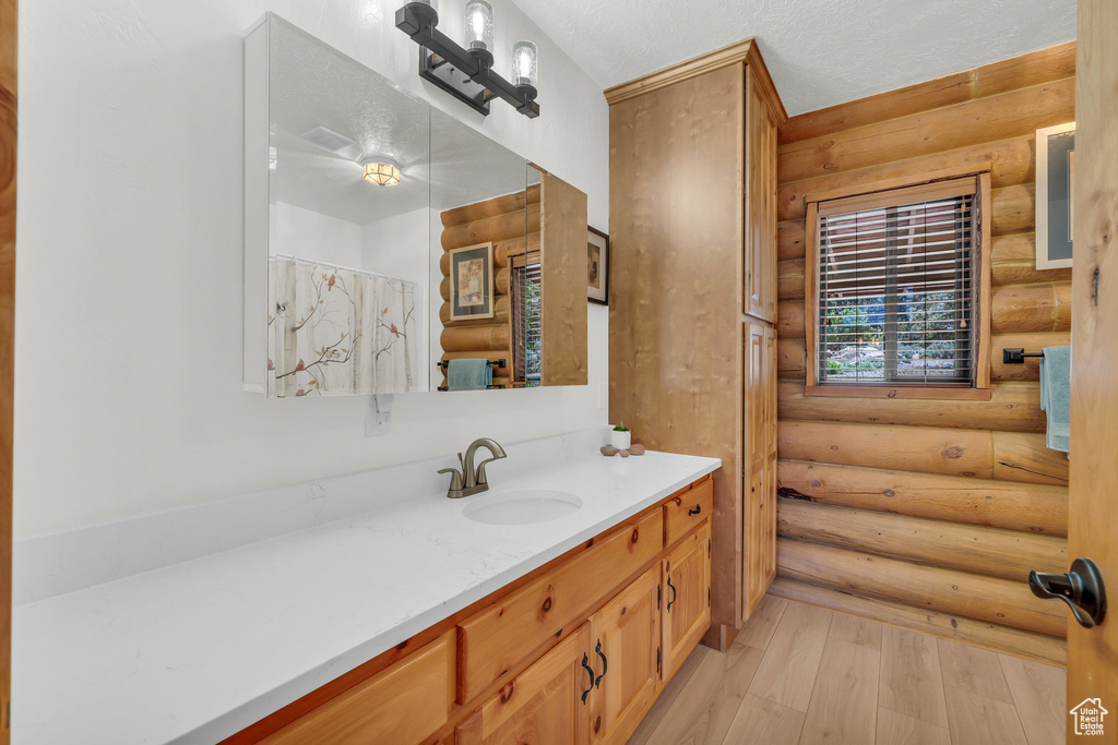 Bathroom featuring a textured ceiling, wood-type flooring, oversized vanity, and log walls