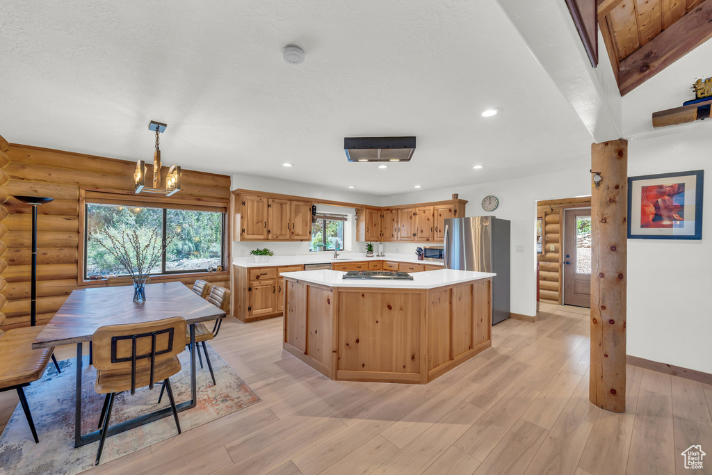 Kitchen with stainless steel appliances, light hardwood / wood-style flooring, decorative light fixtures, and rustic walls