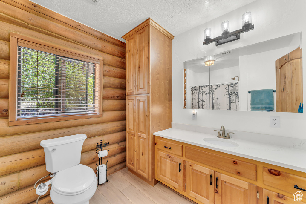 Bathroom featuring a textured ceiling, rustic walls, vanity, and toilet