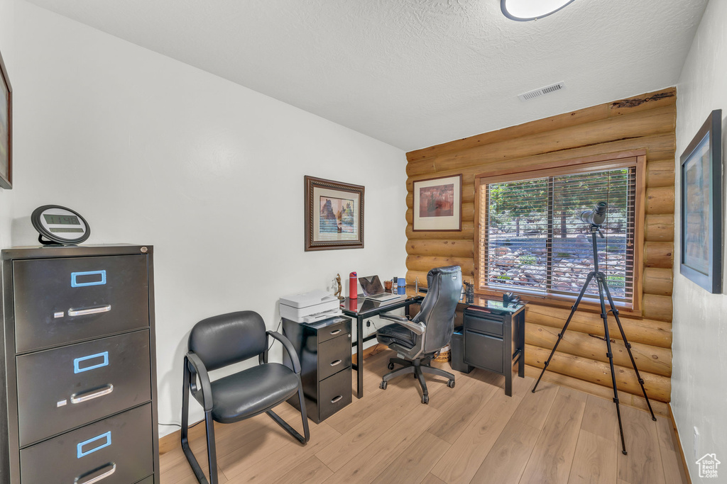 Office space with a textured ceiling, rustic walls, and light hardwood / wood-style flooring